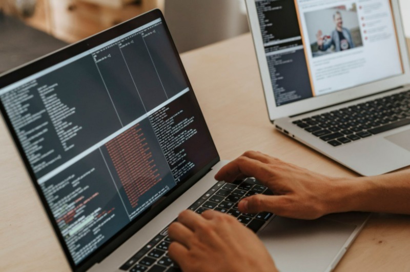 A man typing on one of two laptops