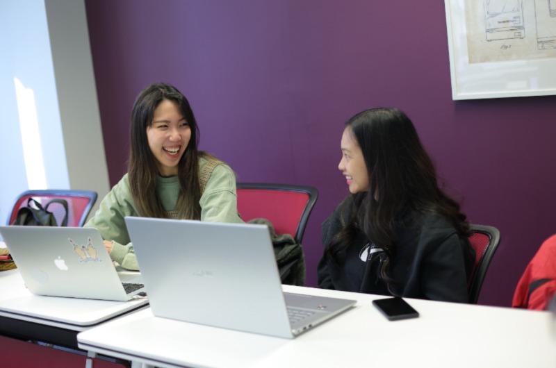 Two women smiling while using a laptop