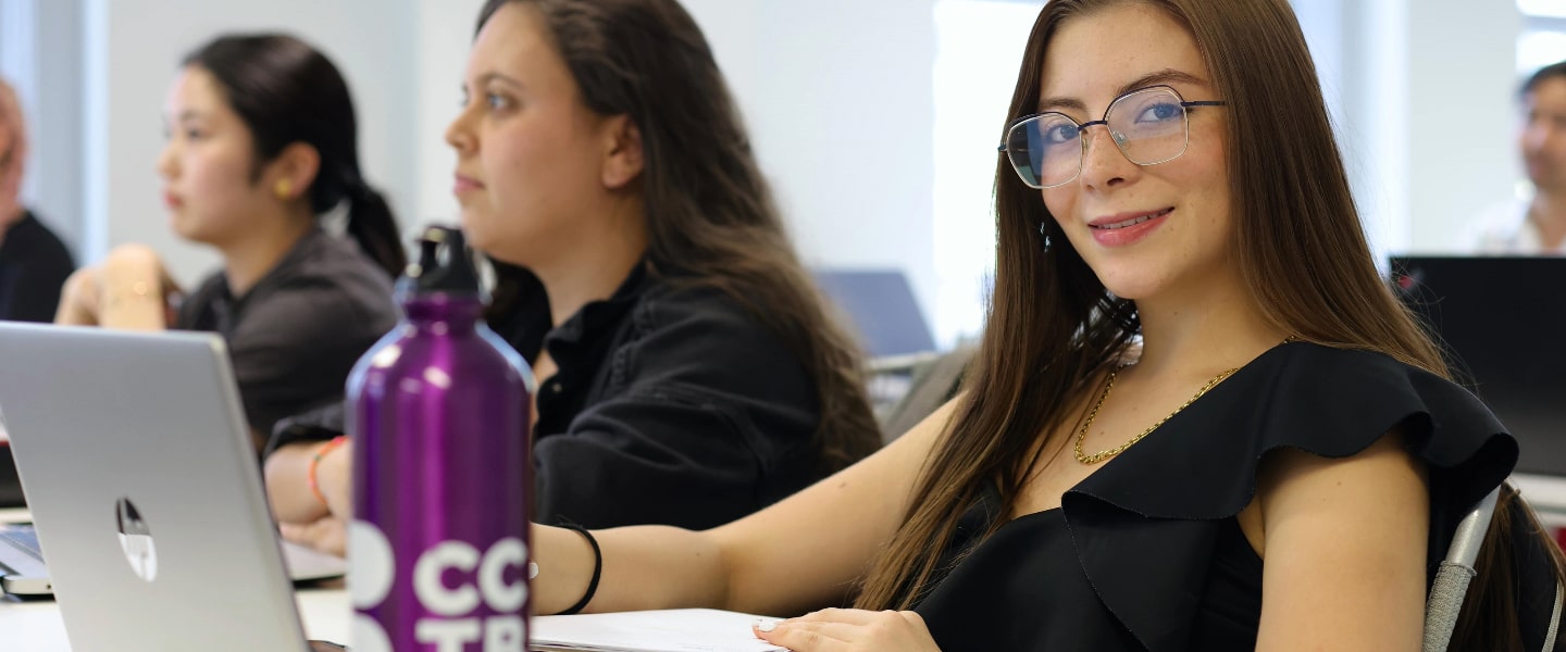 Two girls listening to a lecture, one smiling for a photo
